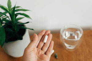 Hand holding magnesium capsule above glass of water on wooden ta