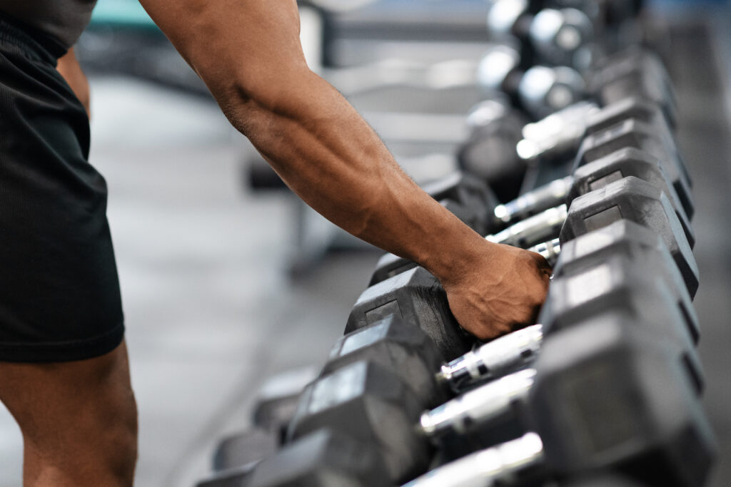 Hand of unrecognizable black guy bodybuilder grabbing dumbbell